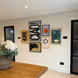 Wall with framed posters and a vase of flowers on a wooden table.