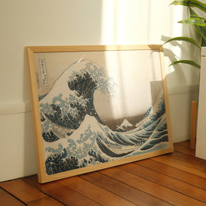 Framed artwork of a wave with Mount Fuji on a wooden floor.